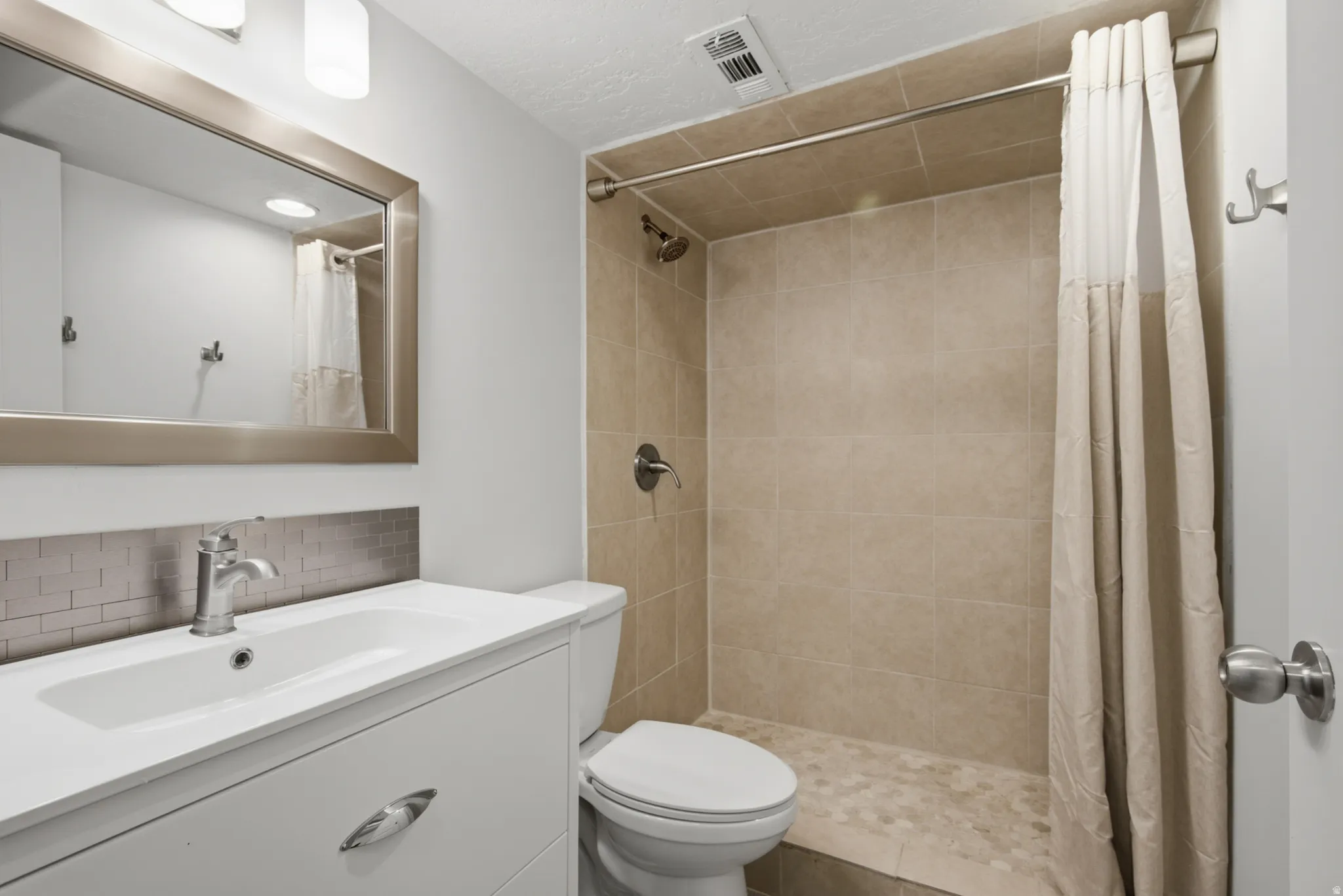 Bathroom featuring a vanity with an integrated sink, brushed metal hardware, and a subway tile backsplash
