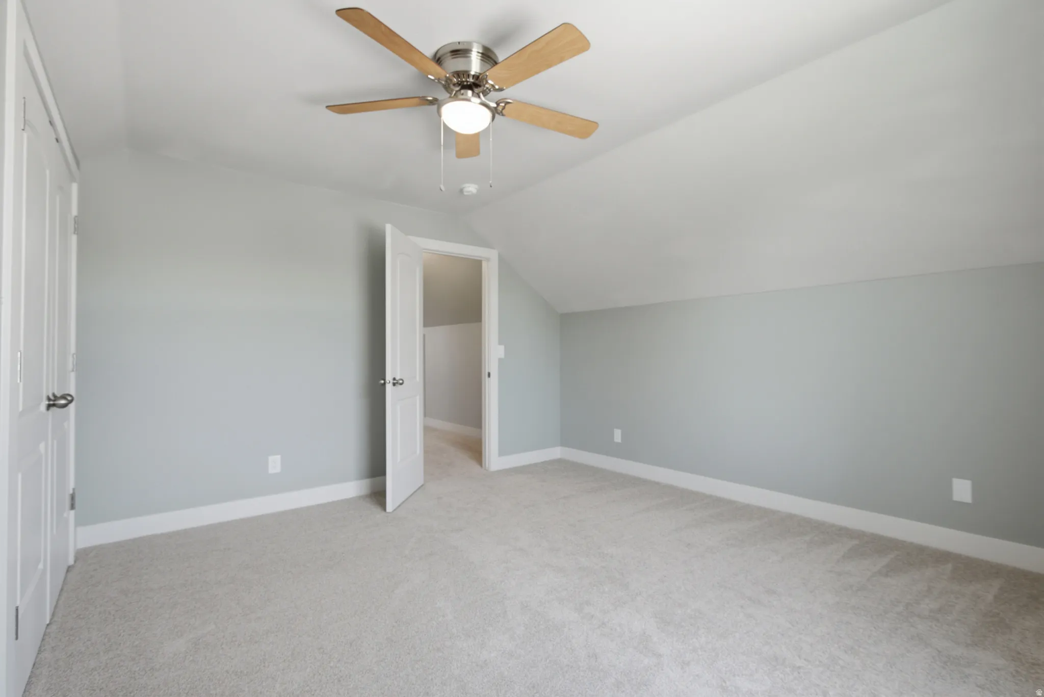 Carpeted room featuring a ceiling fan with wood-finish blades and a light kit, neutral wall paint, white trim, and a white interior door with brushed nickel hardware