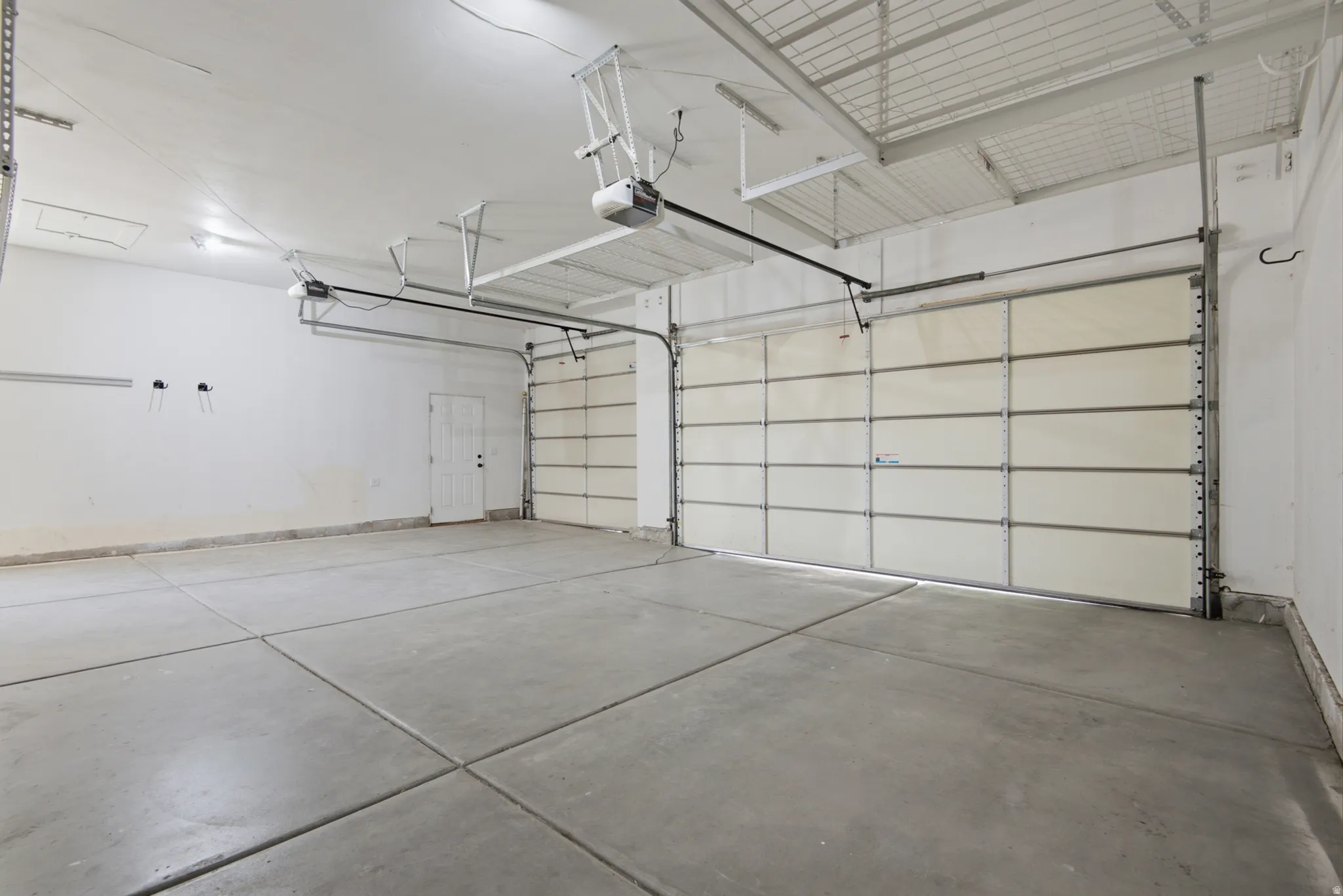 Spacious garage featuring two overhead doors, a pedestrian door, a concrete floor, and overhead lighting