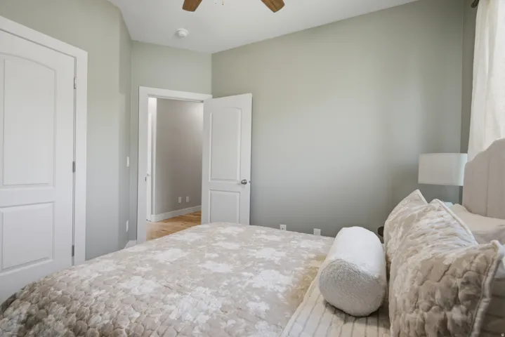 Bedroom featuring light gray wall paint, two white paneled doors, and a ceiling fan with wood-finish blades