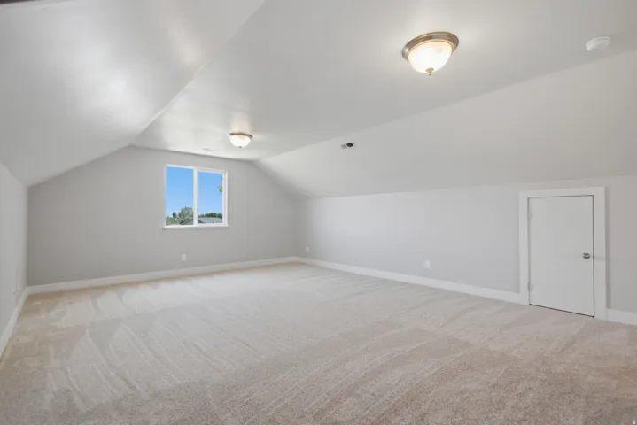 Spacious attic room featuring sloped ceilings, light carpeting, and neutral wall tones