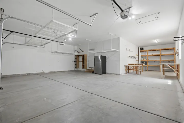Spacious garage featuring a concrete floor, overhead storage racks, exposed shelving, built-in wooden cabinetry, and bright overhead lighting