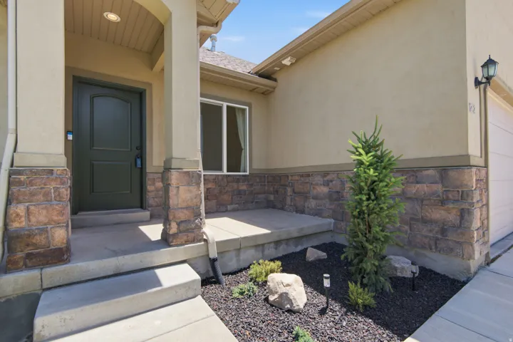 Entryway featuring a dark green paneled door, stone veneer accents, stucco exterior, covered porch, and concrete steps