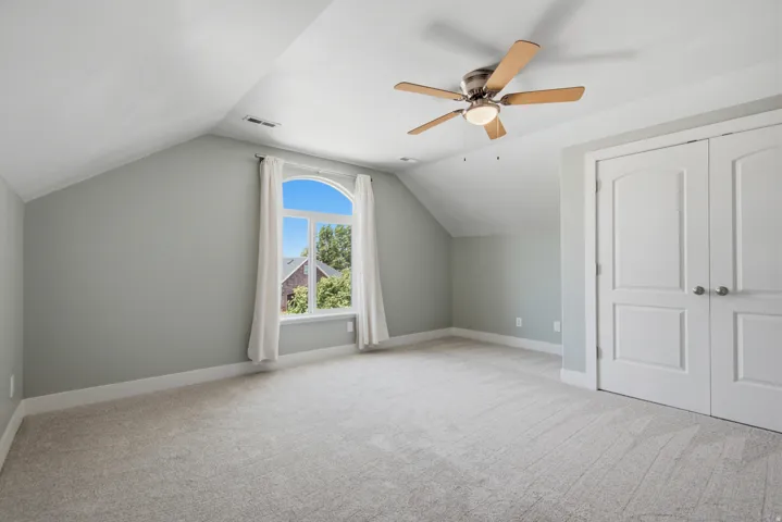 Spacious room featuring vaulted ceilings, light gray wall paint, and plush carpeting