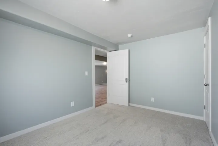 Interior room featuring light gray wall paint, light gray carpet, white baseboards, and white trim around doorways
