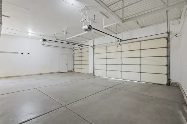 Spacious garage featuring two overhead doors, a pedestrian door, a concrete floor, and overhead lighting