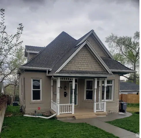 Victorian-style exterior featuring a covered front porch with white railings, a prominent gabled roofline with shingle siding, and a stone foundation
