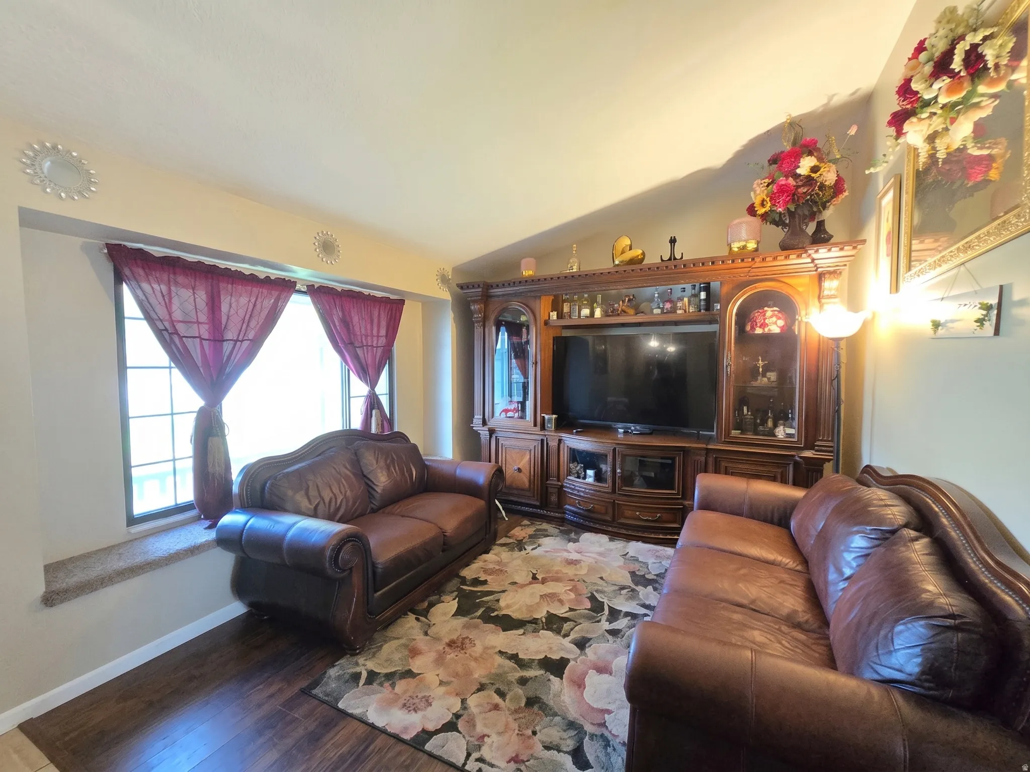 Living area featuring wood-finish flooring, a built-in media console, a window with a sill, and wall-mounted lighting fixtures