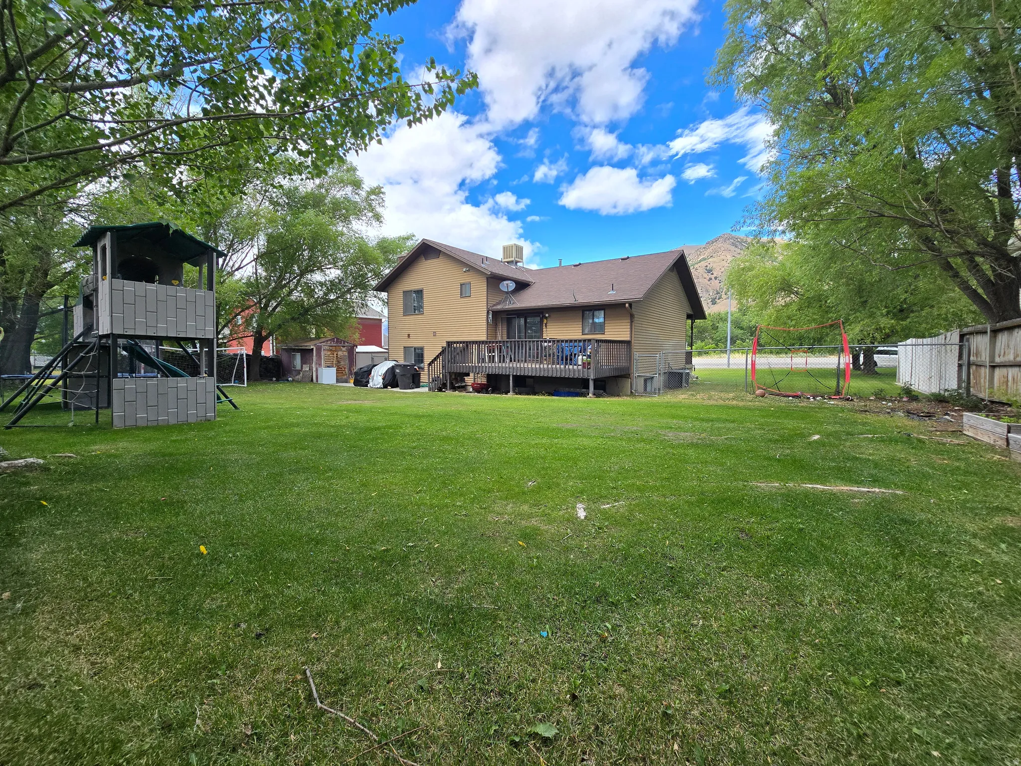 Expansive green lawn with mature trees and a multi-level deck