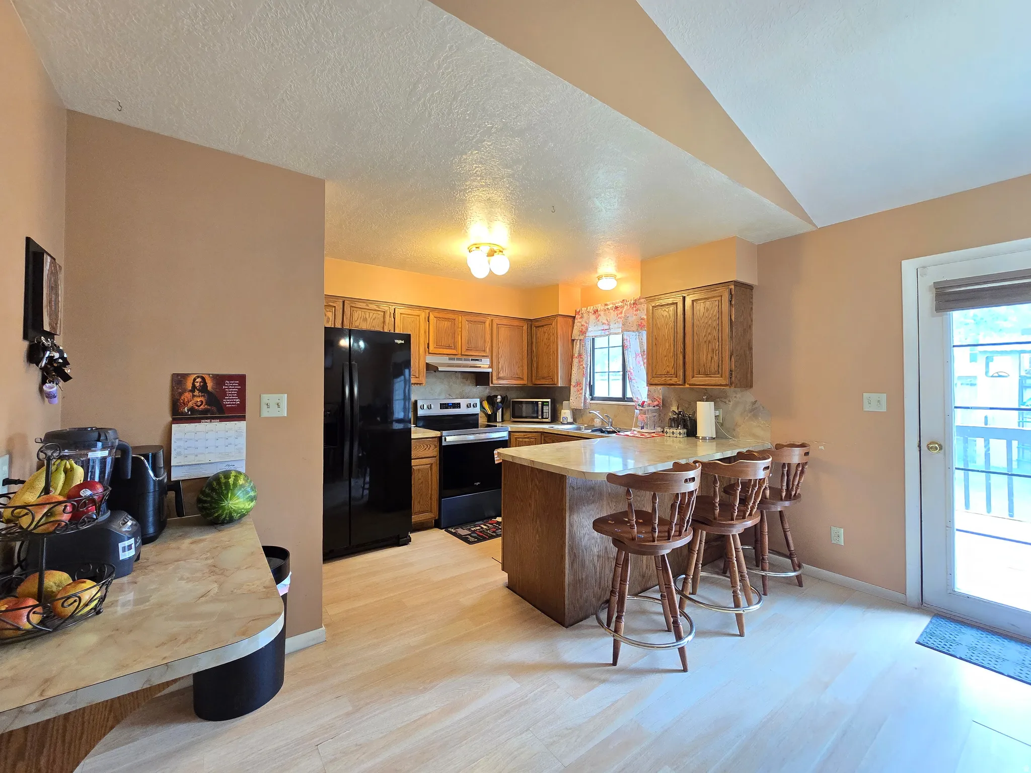 Kitchen featuring light wood-finish flooring, a breakfast bar with seating, wood cabinetry, and a full suite of black appliances