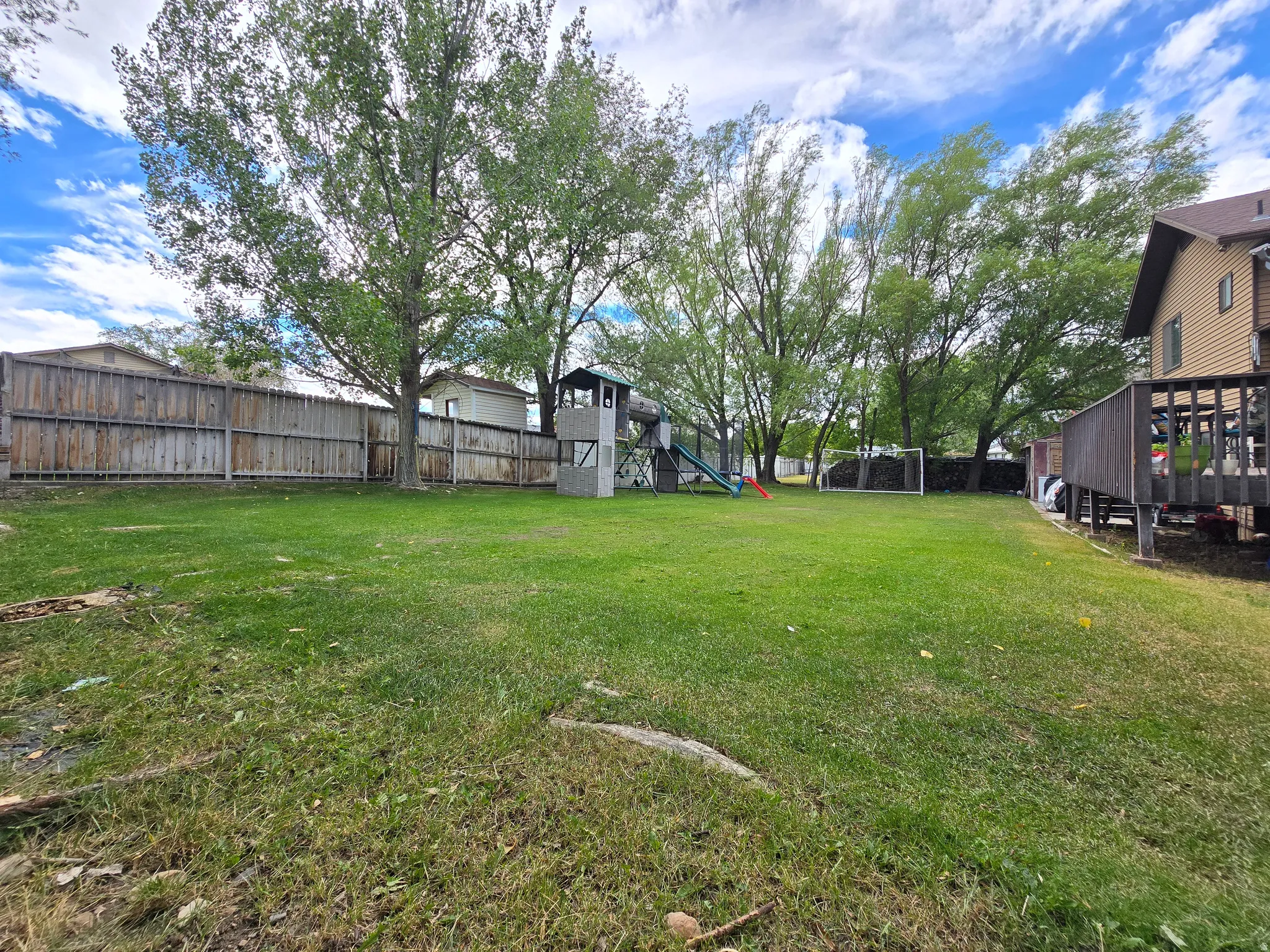 Spacious backyard featuring a manicured lawn, mature trees, a privacy fence, and a raised wood deck