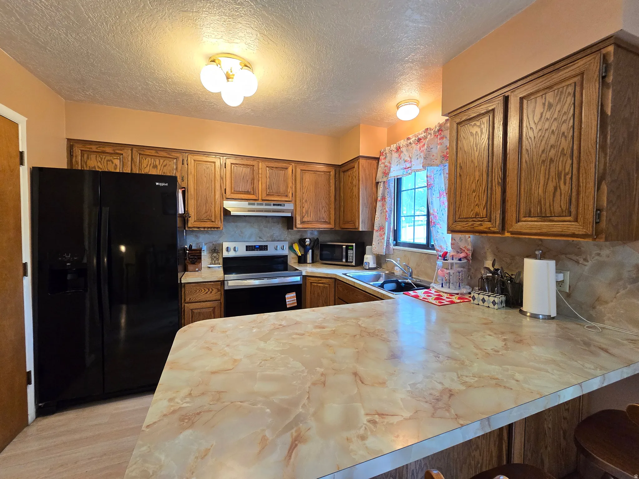 Kitchen featuring wood-finish cabinetry, a black side-by-side refrigerator, and a stainless steel range
