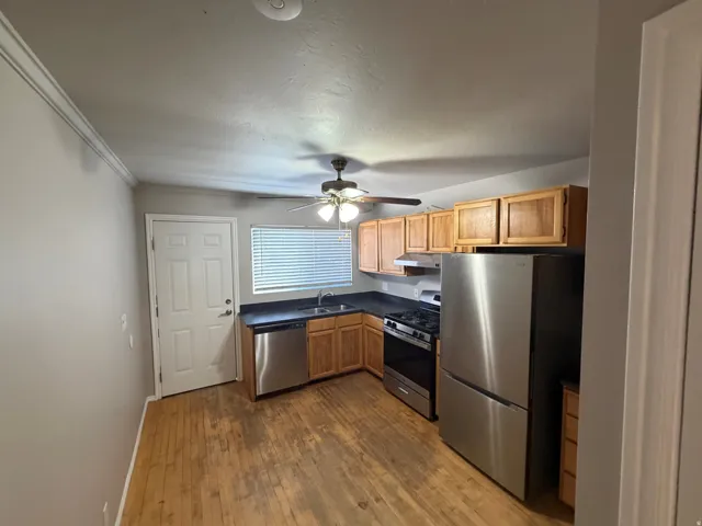 Kitchen featuring wood-finish flooring, stainless steel appliances, wood cabinetry, and a ceiling fan with integrated lighting