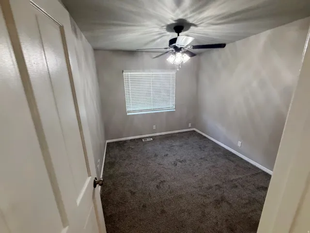 Neutral-toned room featuring a ceiling fan with integrated lighting, a window with horizontal blinds, gray wall-to-wall carpeting, and white baseboards