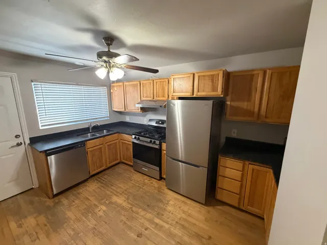 Kitchen featuring wood-finish flooring, stainless steel appliances, dark countertops, and wood cabinetry