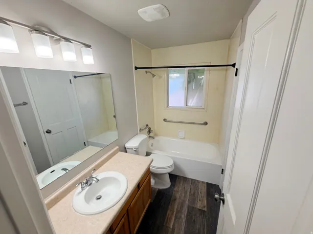 Full bathroom with wood-finish flooring, a vanity with a laminate countertop, and a white porcelain sink