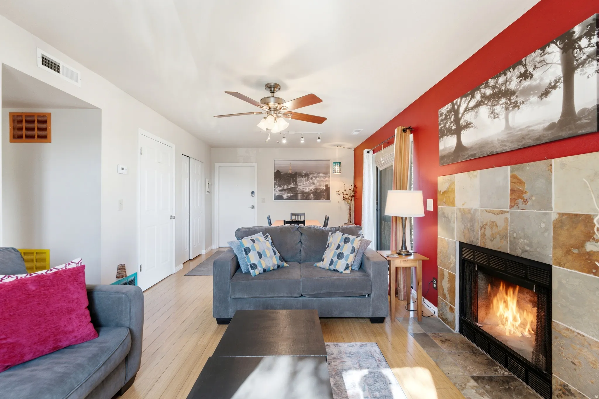Living area featuring a fireplace with stone tile surround, wood-finish flooring, a ceiling fan, and a red accent wall