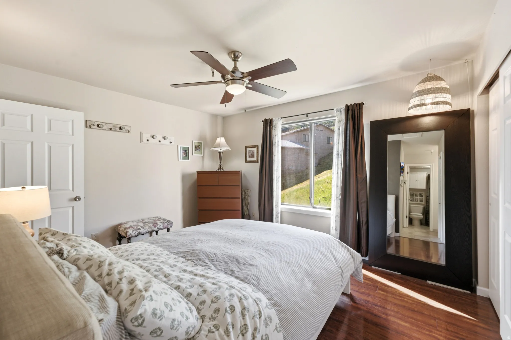 Bedroom featuring rich wood-finish flooring, a ceiling fan with integrated lighting, and a window with a green landscape backdrop