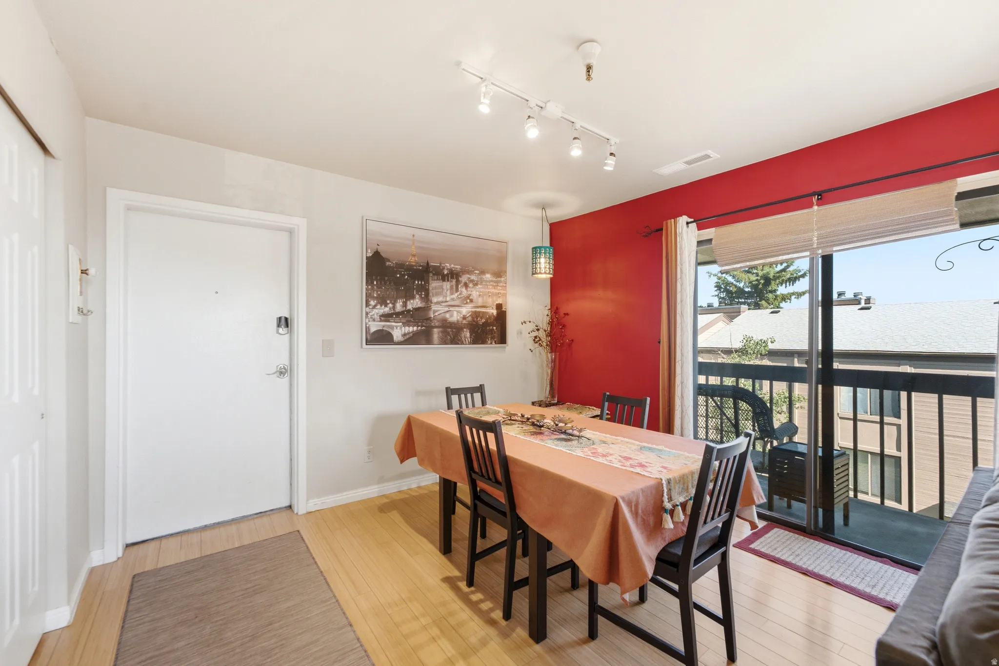 Dining area featuring wood-finish flooring, a vibrant accent wall, and a sliding glass door leading to an exterior balcony with black railings