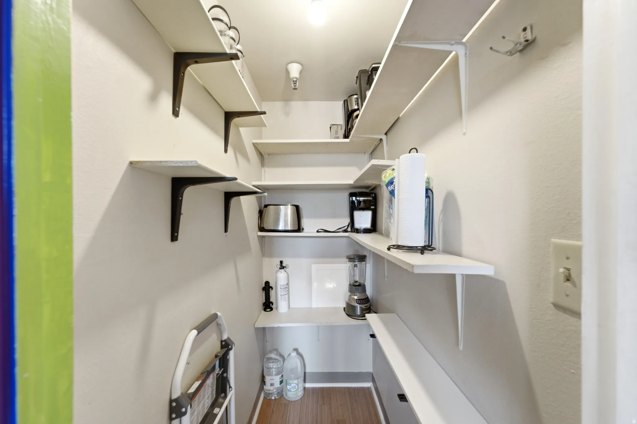 Walk-in pantry featuring extensive open shelving, a built-in countertop, and wood-finish flooring