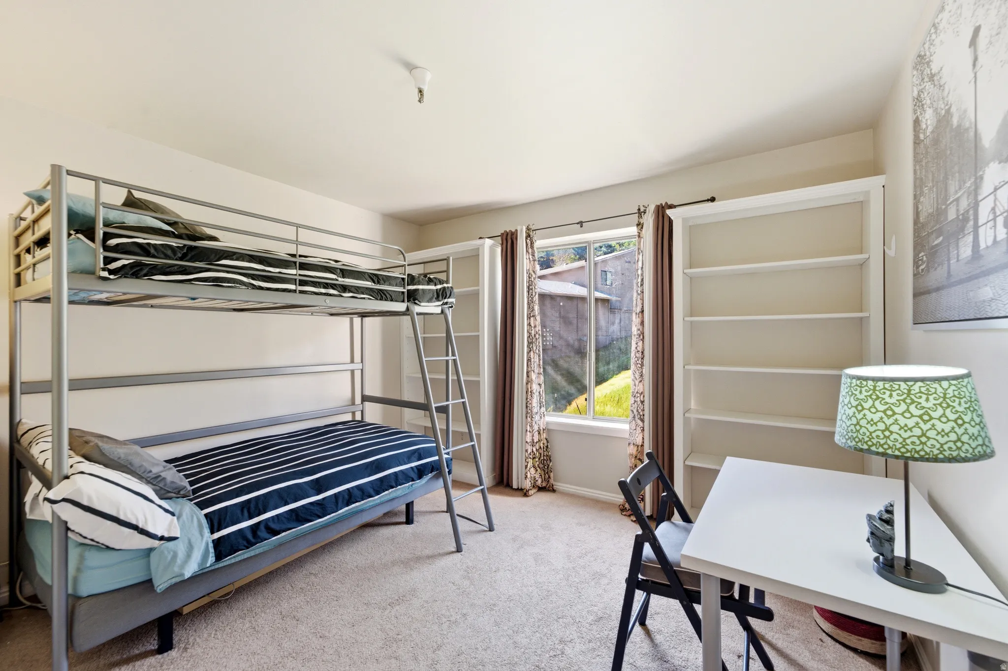 Carpeted room featuring a window with patterned drapes, a built-in shelving unit, and neutral wall tones