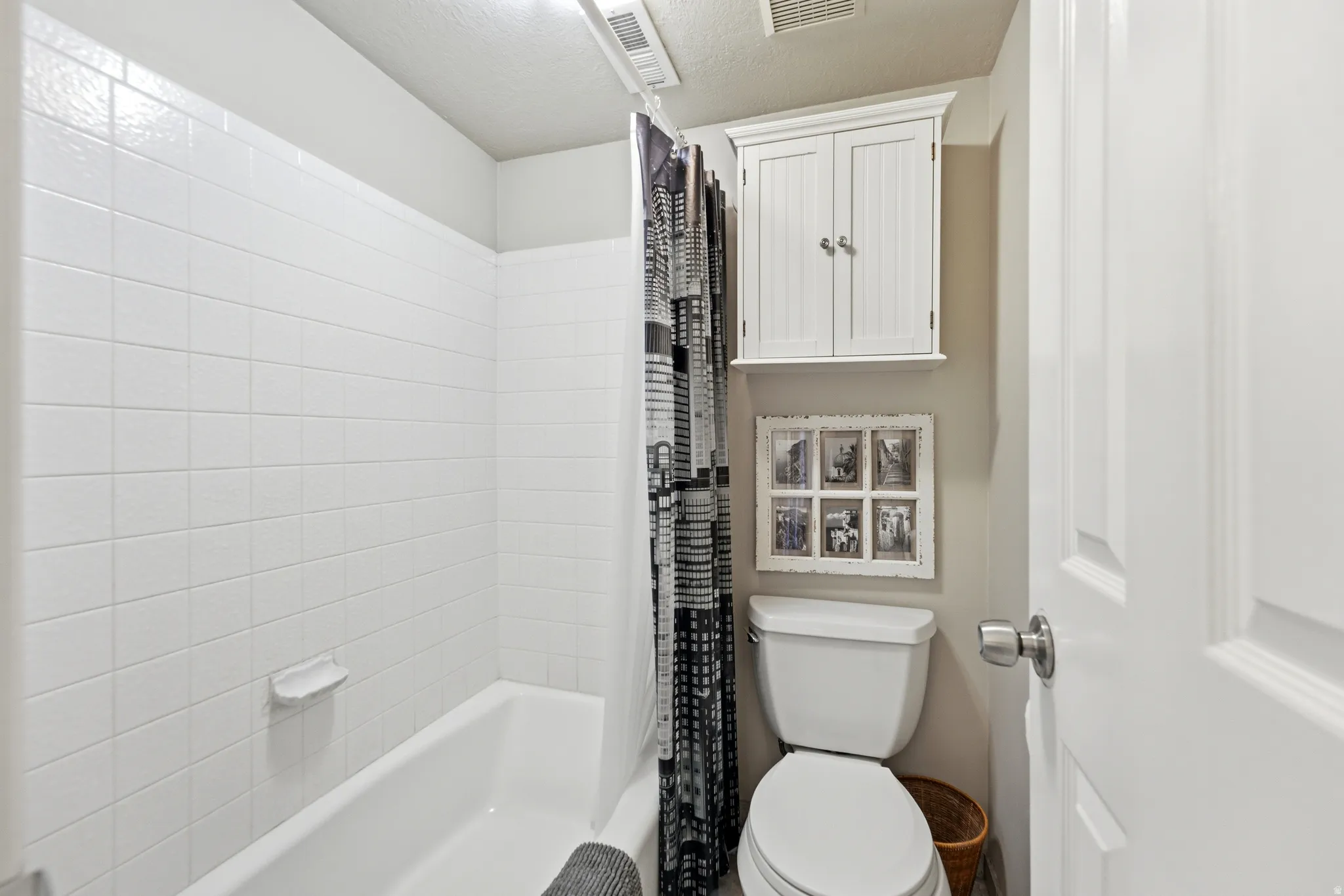 Bathroom featuring a white bathtub with subway tile surround, white toilet, and a wall-mounted white storage cabinet