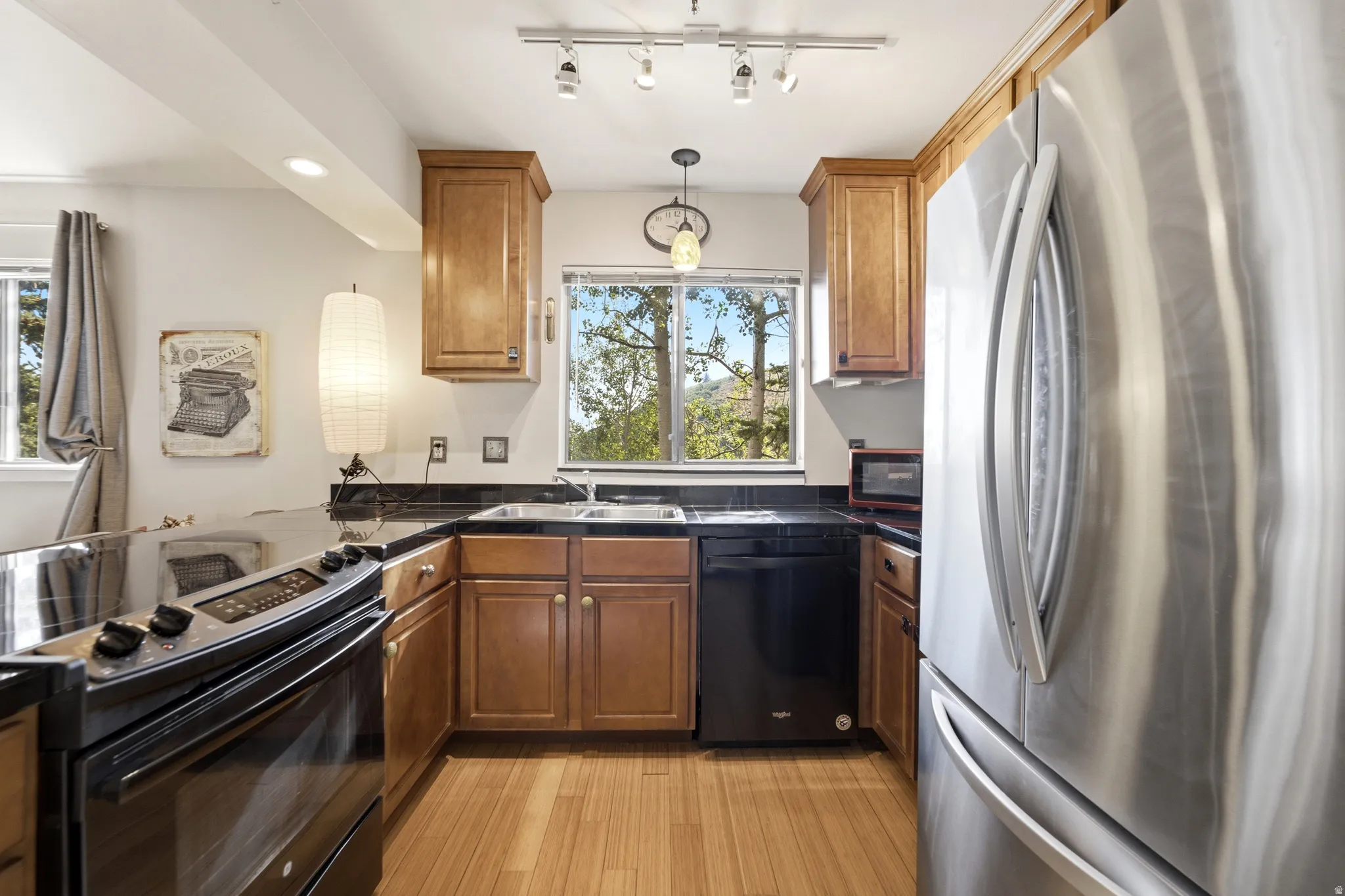 Kitchen featuring wood-finish flooring, dark countertops, wood cabinetry, a stainless steel refrigerator, and a black range