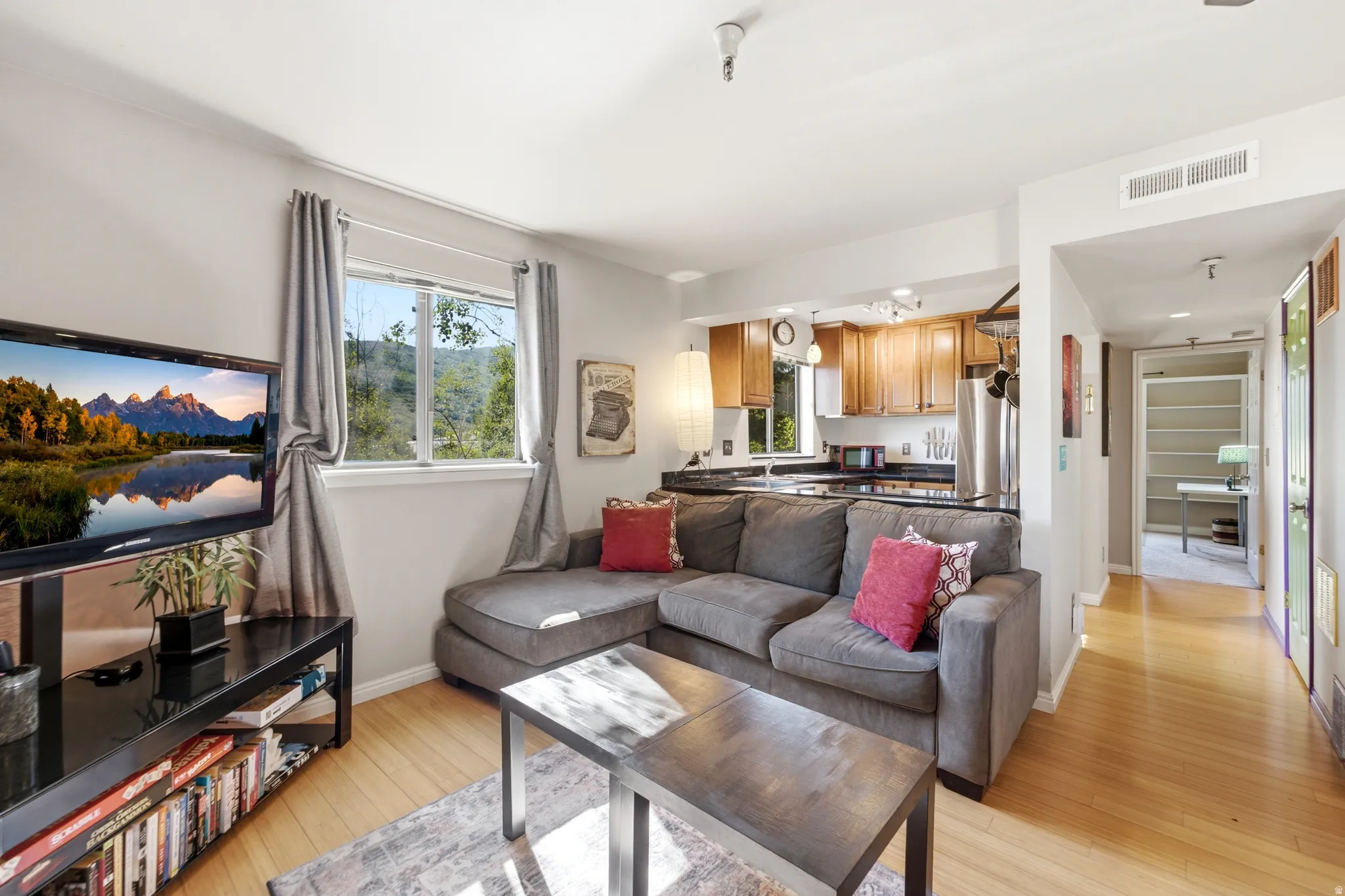 Open-concept living area featuring light wood-finish flooring, a window with outdoor scenery, and a kitchen with wood cabinetry and black countertops