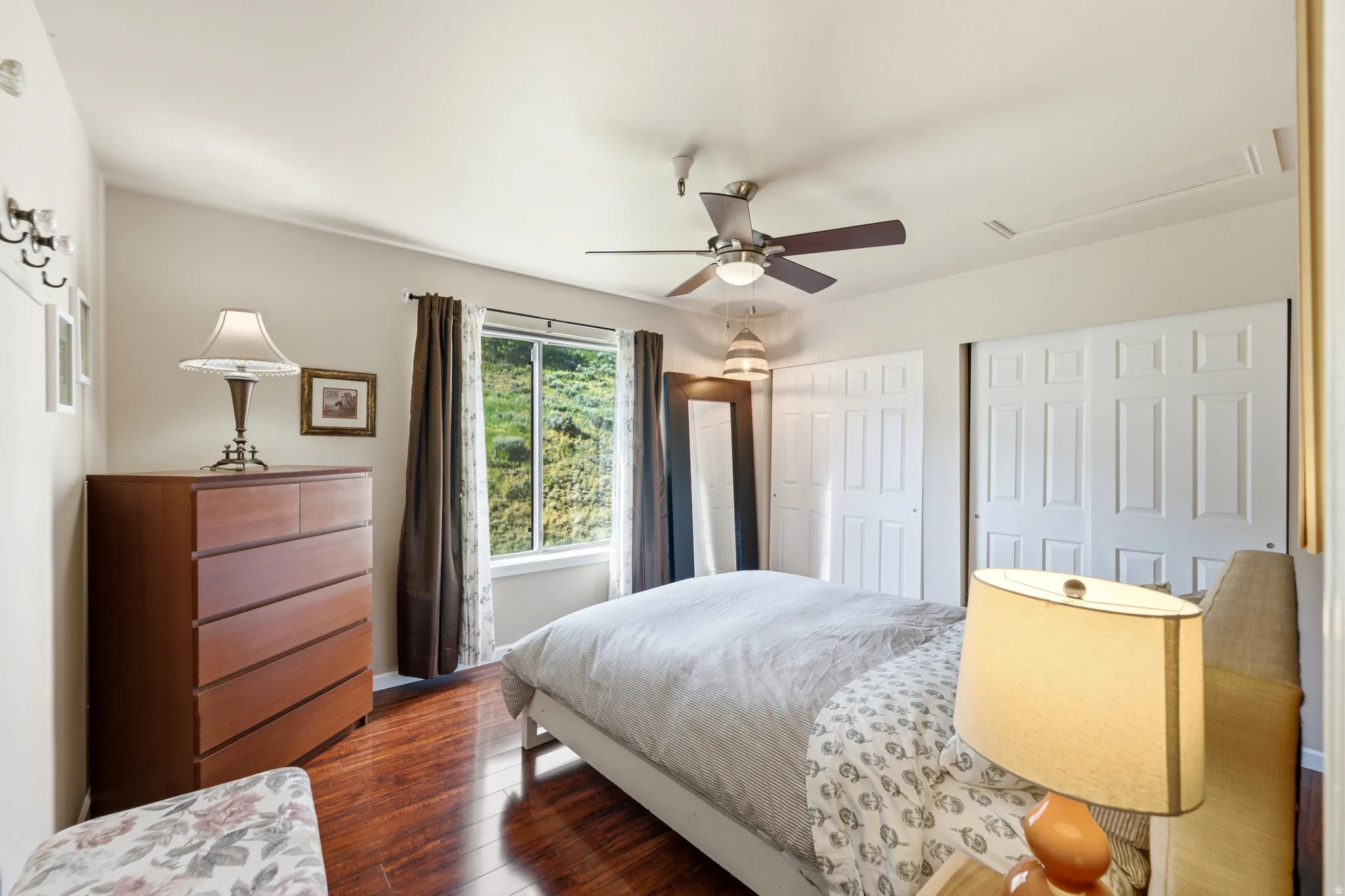 Bedroom featuring wood-finish flooring, a window with natural light, a ceiling fan with integrated lighting, and two sets of bi-fold closet doors