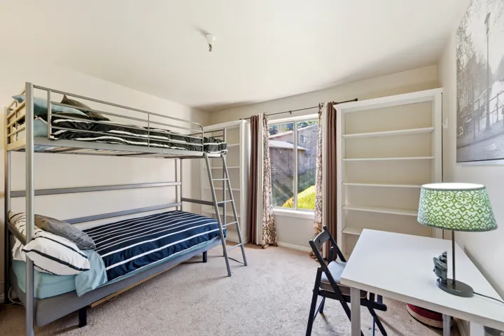 Carpeted room featuring a window with patterned drapes, a built-in shelving unit, and neutral wall tones