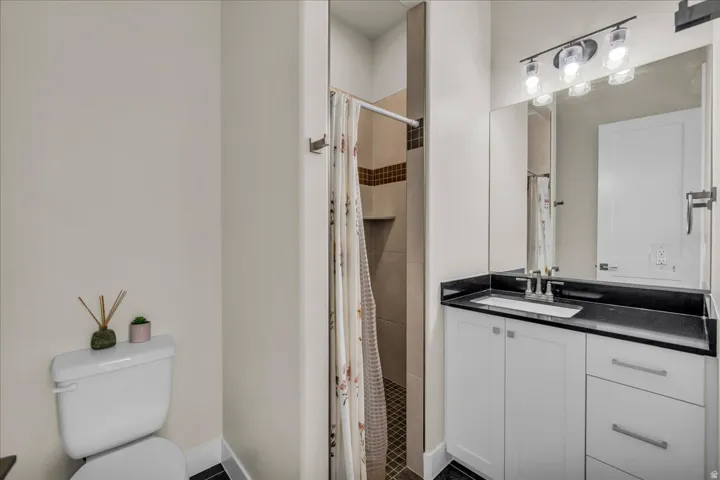 Bathroom featuring a white vanity with a black countertop, a built-in sink, a wall-mounted mirror, and a shower with tiled walls and a recessed niche