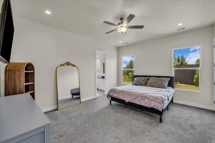 Carpeted bedroom featuring two large windows, a ceiling fan with integrated lighting, and recessed ceiling lights