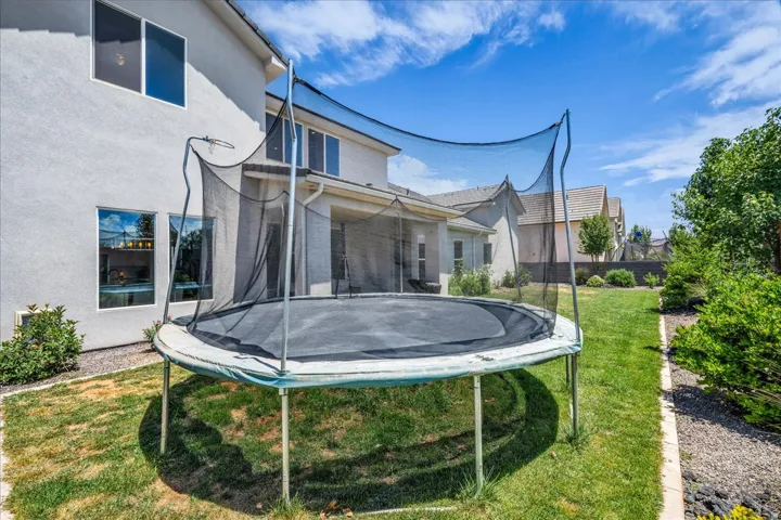 Spacious backyard featuring a covered patio, stucco exterior, multiple large windows, mature landscaping, and a manicured lawn