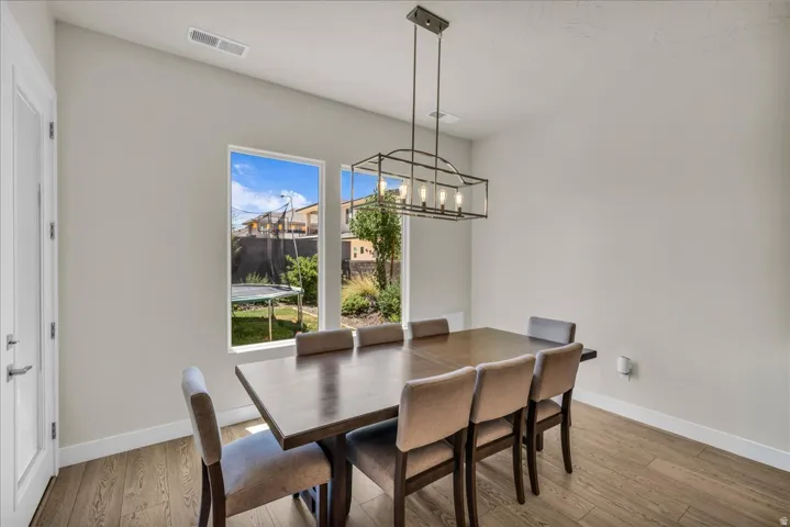 Dining area featuring wood-finish flooring, a modern linear chandelier, and a large window overlooking the backyard