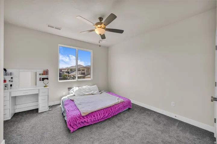 Bedroom featuring neutral wall paint, gray carpeting, a multi-pane window, and a ceiling fan with integrated lighting