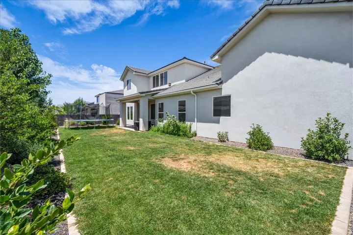 Expansive backyard featuring a manicured lawn, established perimeter greenery, and a two-story stucco exterior