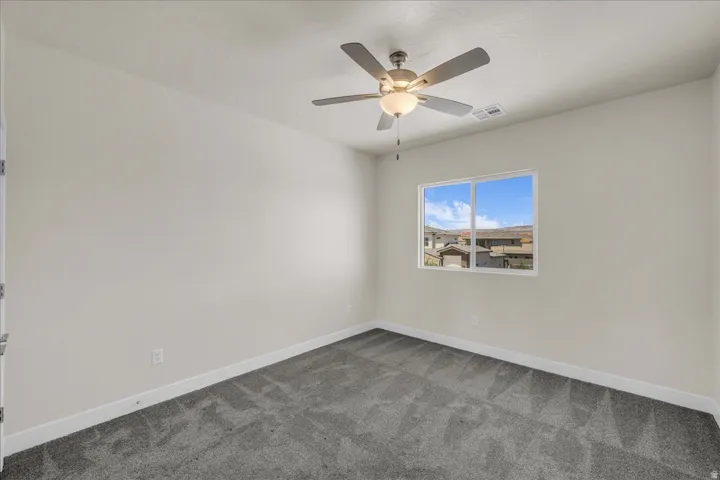 Neutral-toned room featuring a ceiling fan with integrated lighting, a double-paned window, and plush gray carpeting