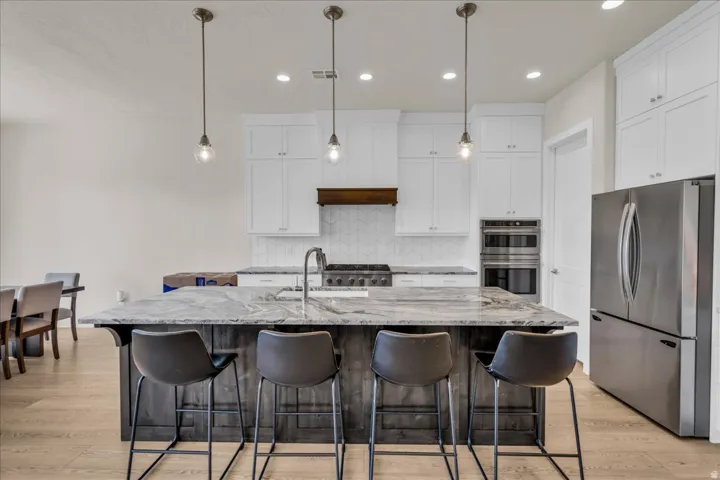 Gourmet kitchen featuring a large island with a stone countertop, white upper cabinetry, stainless steel appliances, and wood-finish flooring
