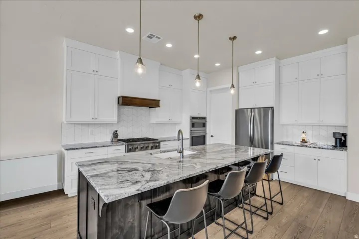 Gourmet kitchen featuring a large central island with seating, white shaker cabinetry, stainless steel appliances, and wood-finish flooring
