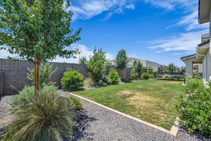 Private backyard featuring a block wall perimeter, mature trees, landscaped gravel beds, and a grassy expanse