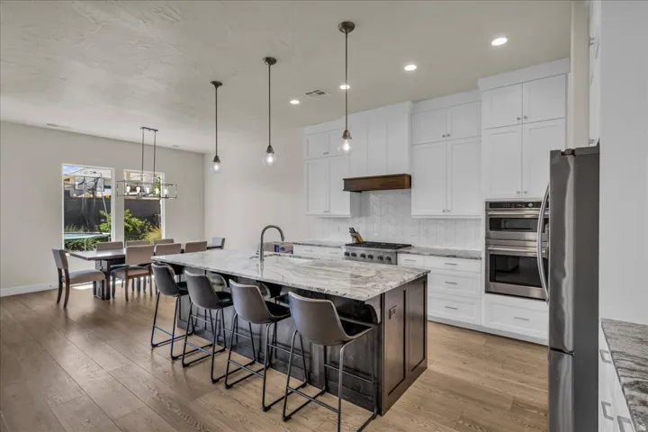 Gourmet kitchen with a large island featuring a stone countertop, white shaker cabinetry, stainless steel appliances, and wood-finish flooring