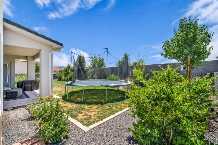 Rear yard with a covered patio featuring a built-in outdoor grill, a gravel perimeter, mature landscaping, and a block wall fence