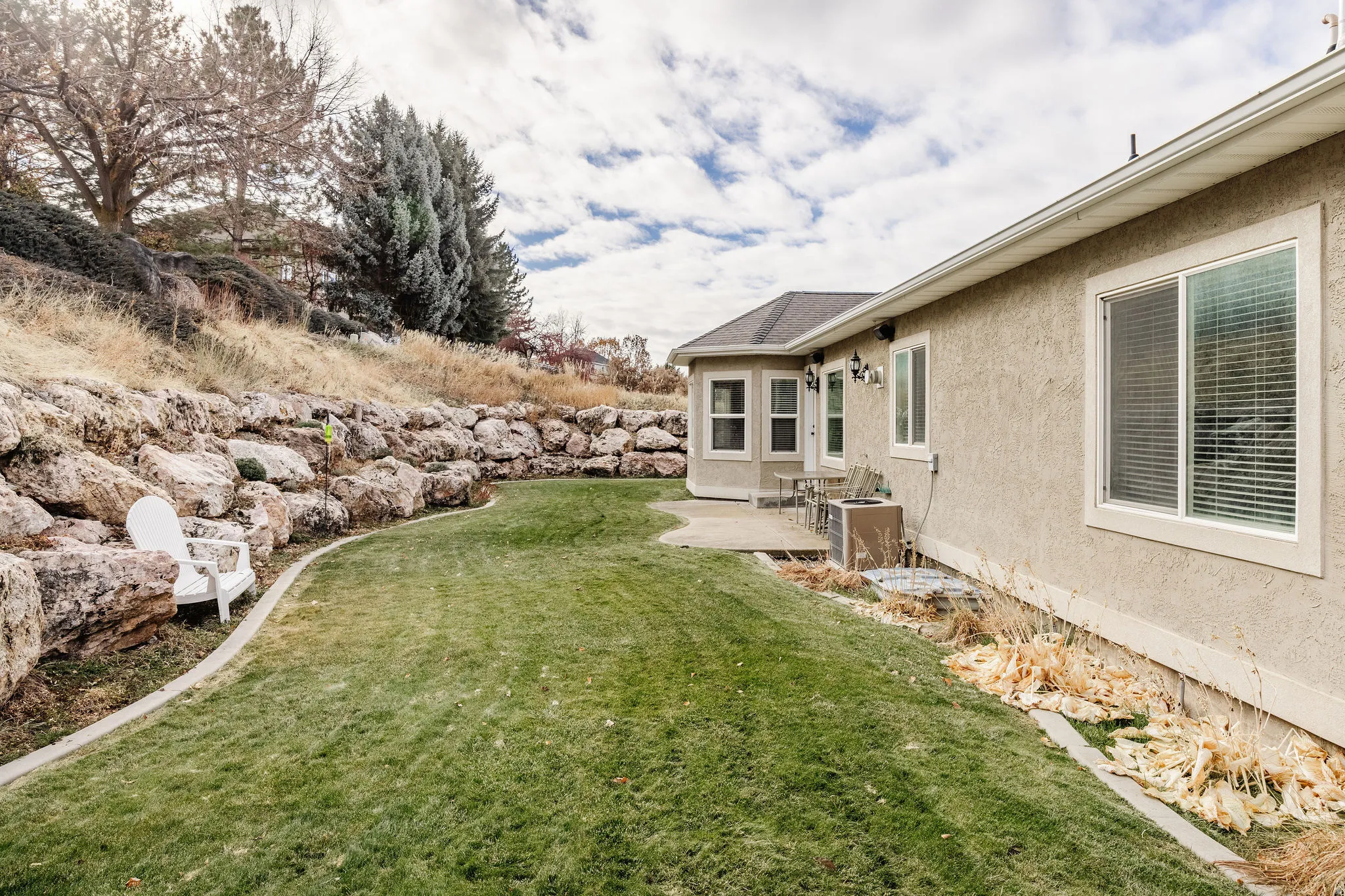 Expansive backyard featuring a manicured lawn, a large stone retaining wall, and a concrete patio