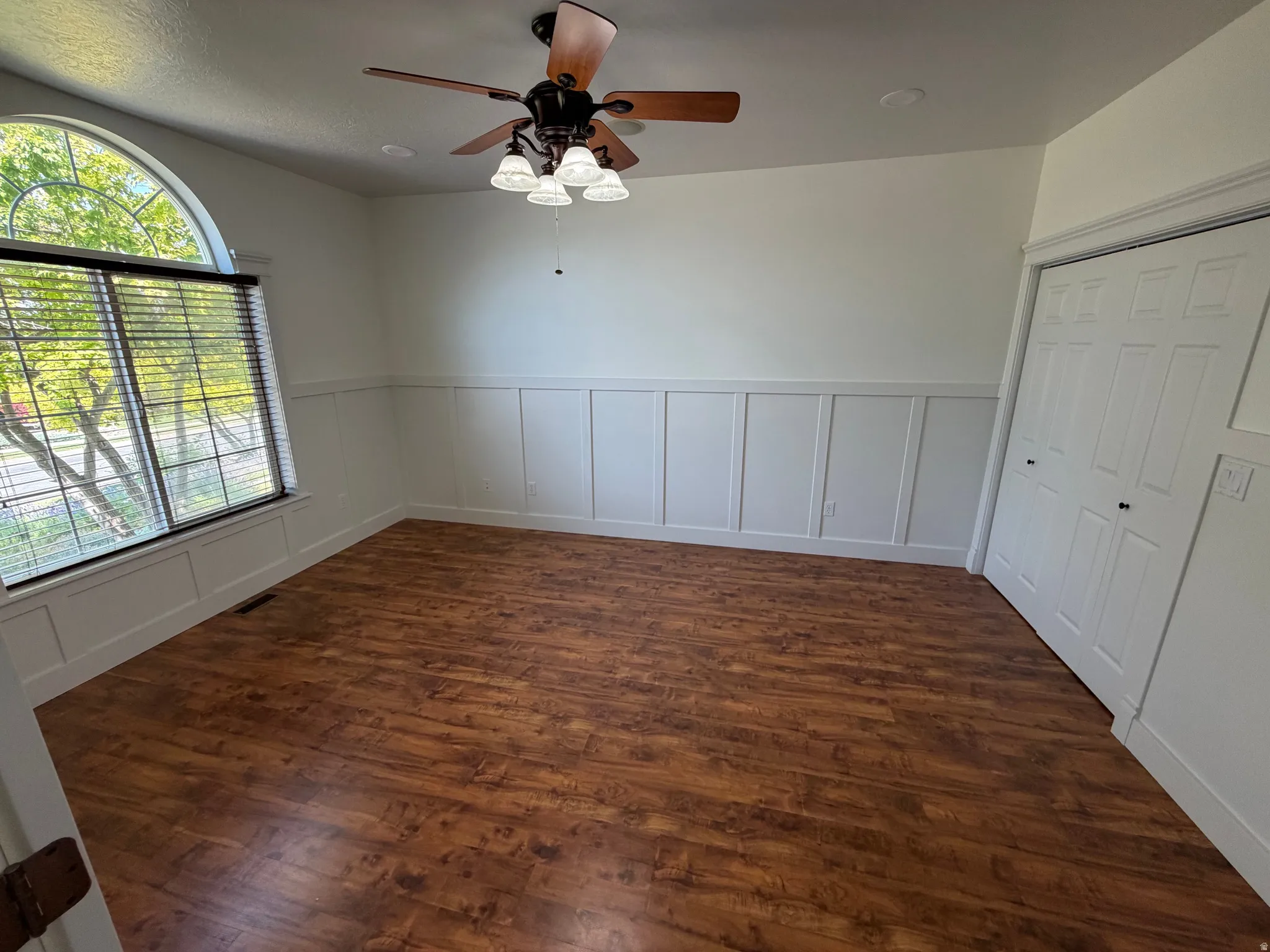 Room featuring wood-finish flooring, white board and batten wall detailing, and a multi-pane arched window with blinds