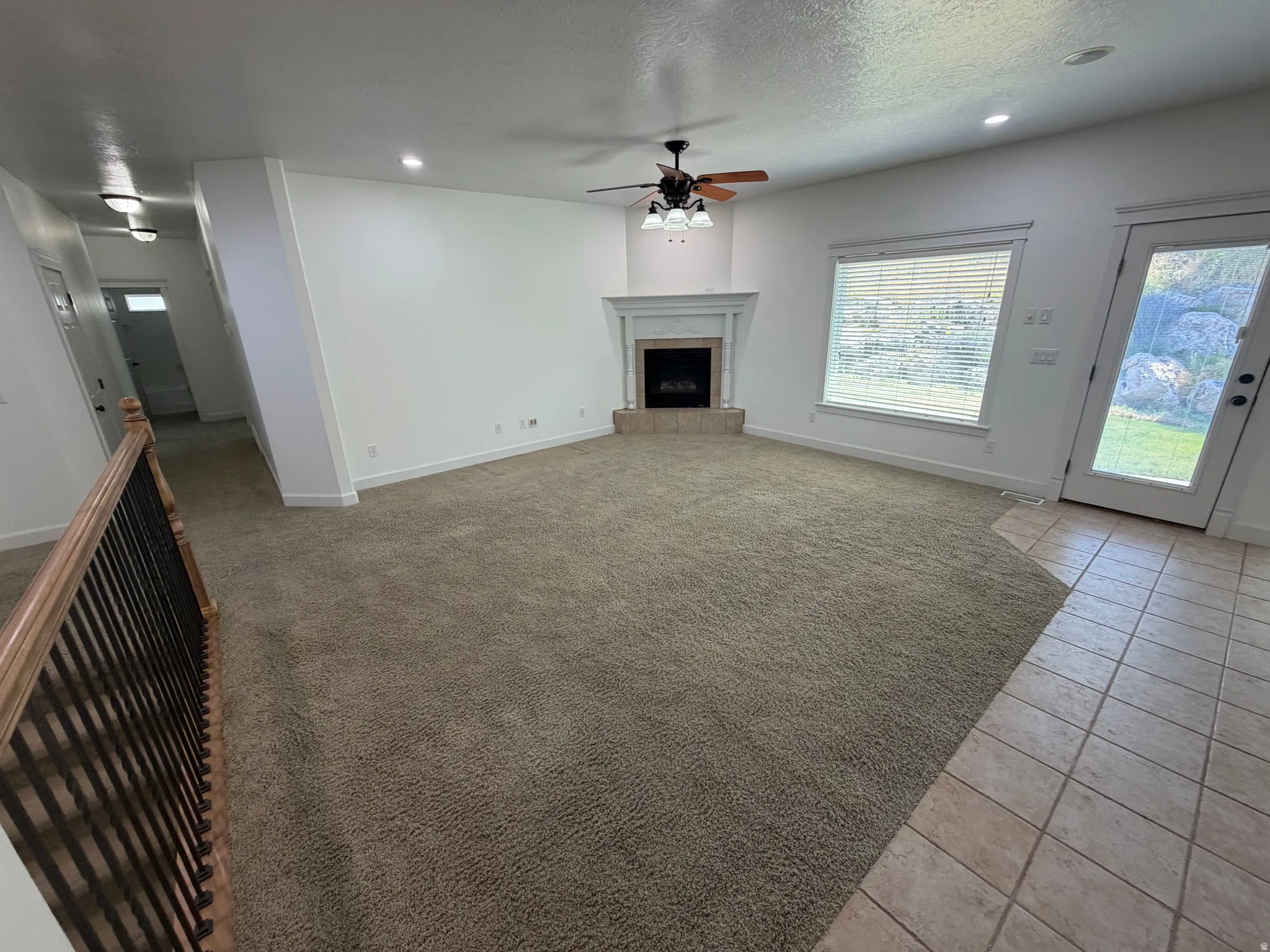 Spacious carpeted living area with a corner fireplace featuring a white mantle and hearth