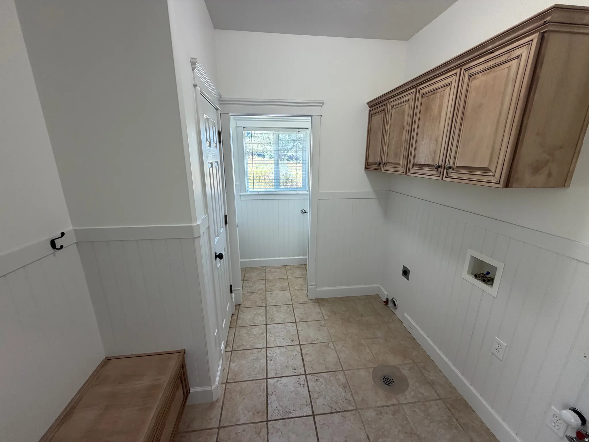 Utility space featuring light wood-finish cabinetry, wainscoting, and tile flooring