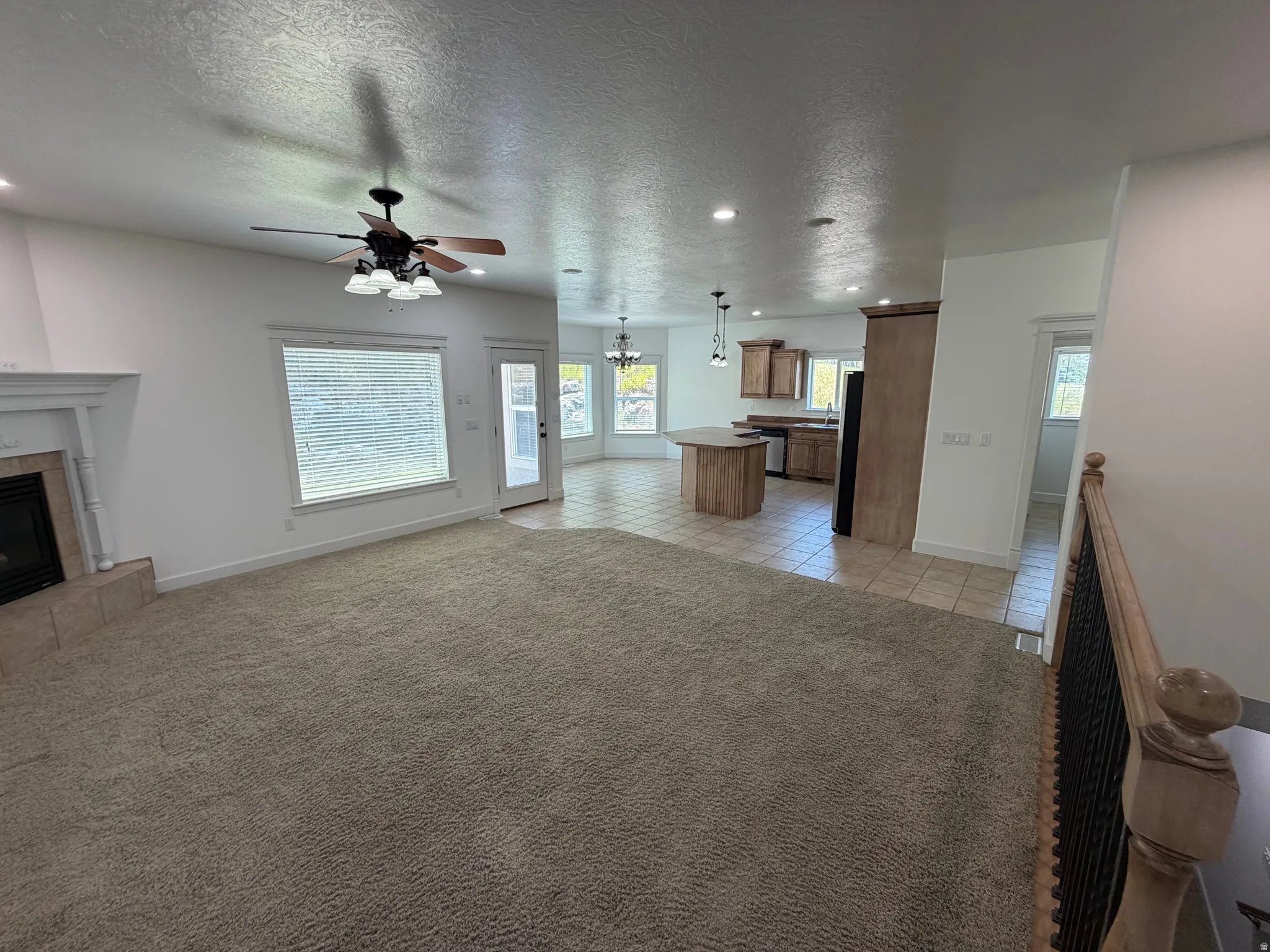 Open-concept living area featuring a fireplace with a decorative mantel, ceiling fan with integrated lighting, and multiple windows