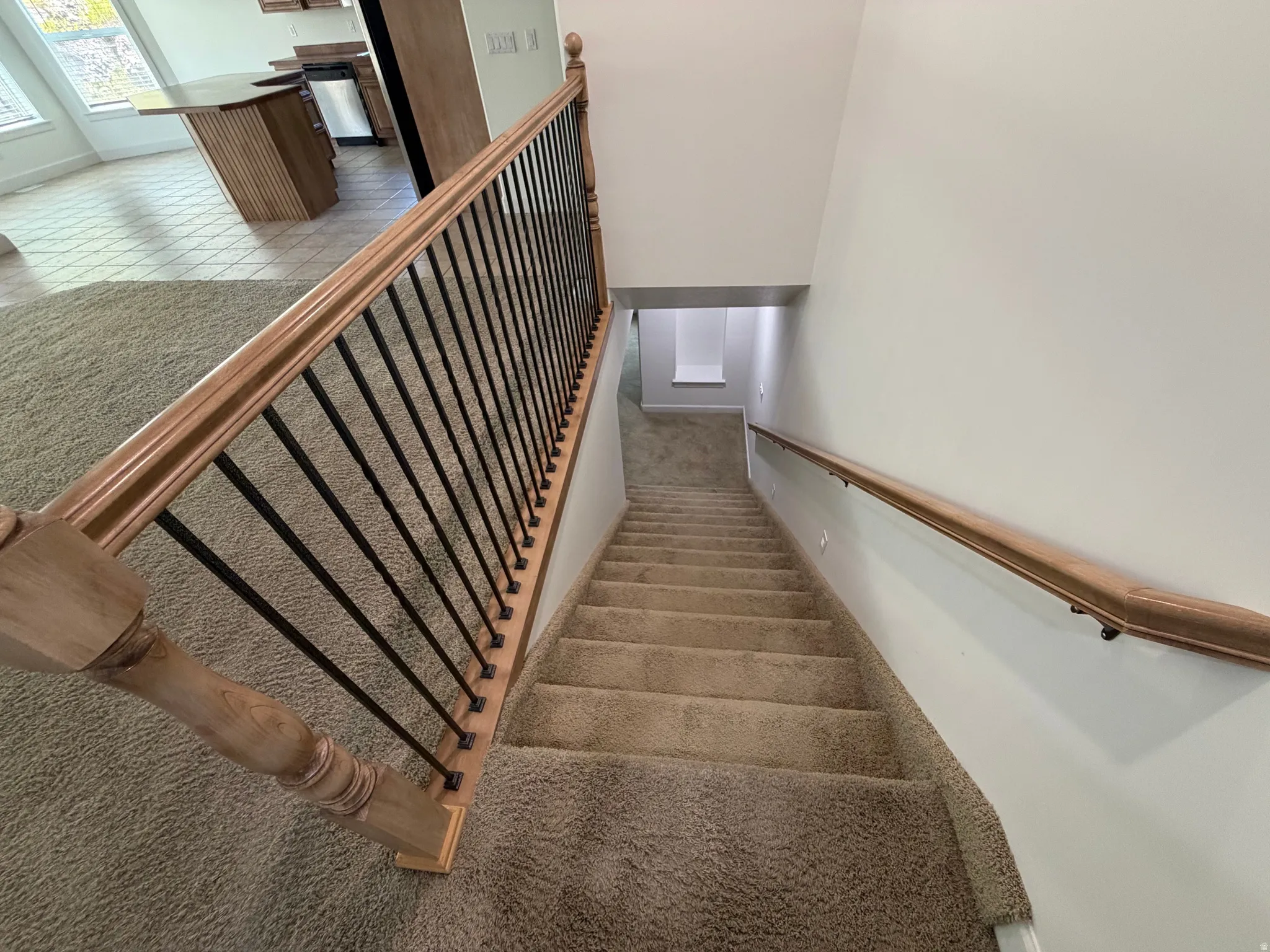Carpeted staircase with light wood-finish handrails and black metal balusters