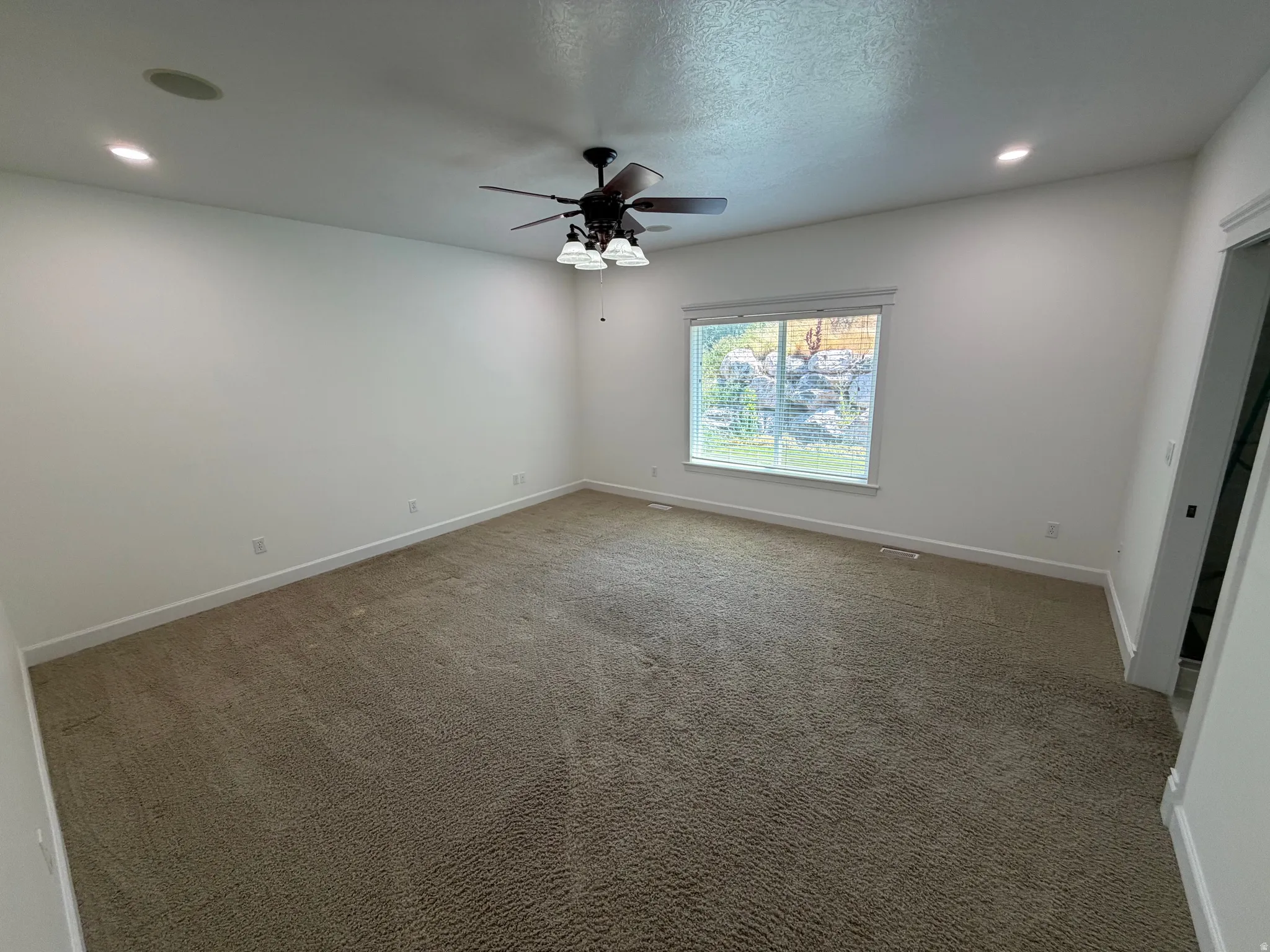 Spacious room featuring neutral carpeting, white walls, and a large window with white blinds