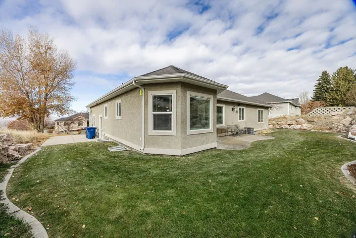 Rear exterior featuring a stucco facade, multiple windows with white trim, and a patio area